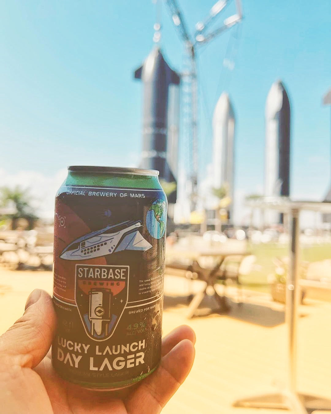Someone enjoying a can of Starbase Brewing Lucky Launch Day Lager up in front of the Rocket Garden at Starbase